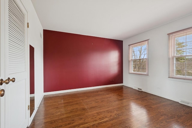 spare room with wood finished floors, visible vents, and baseboards