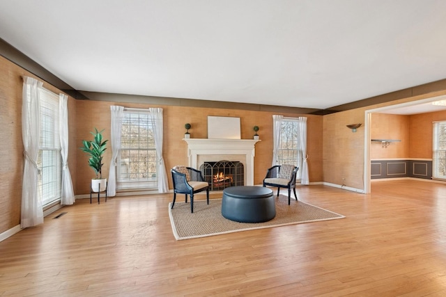 living area featuring light wood-style floors, visible vents, a warm lit fireplace, and baseboards