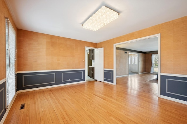 empty room featuring visible vents, wallpapered walls, a wainscoted wall, and wood finished floors