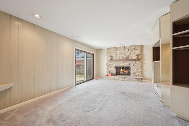 unfurnished living room featuring a stone fireplace, recessed lighting, baseboards, and light carpet