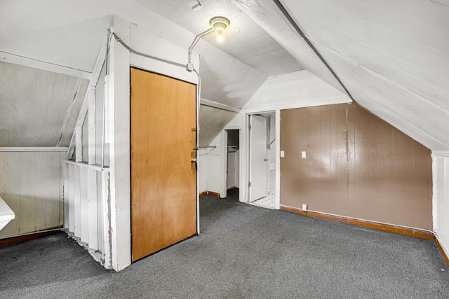 bonus room with vaulted ceiling, wood walls, and carpet