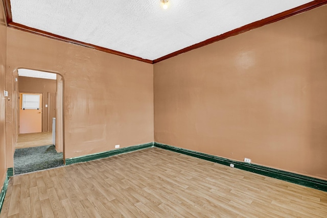 unfurnished room with a textured ceiling, arched walkways, crown molding, and wood finished floors