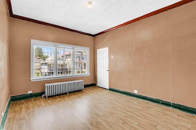 empty room with ornamental molding, radiator heating unit, wood finished floors, and baseboards