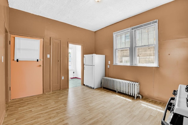 kitchen with freestanding refrigerator, radiator, a textured ceiling, and light wood finished floors