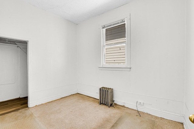 unfurnished room with a textured ceiling, radiator heating unit, and carpet