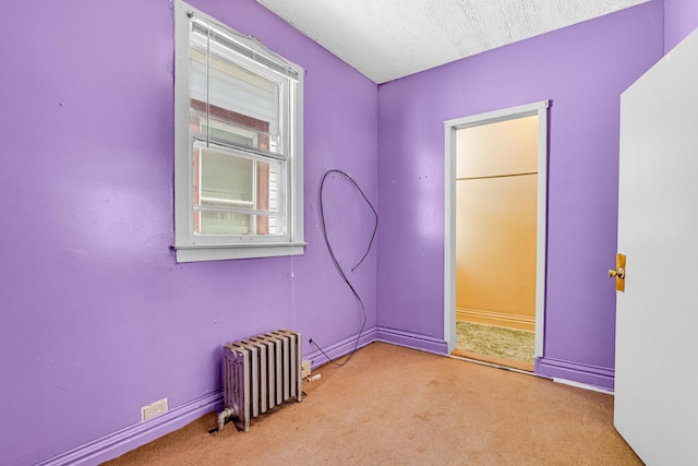 carpeted spare room with a textured ceiling, baseboards, and radiator