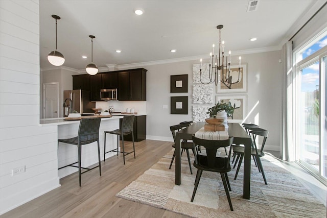 dining room featuring ornamental molding, light wood-type flooring, visible vents, and baseboards