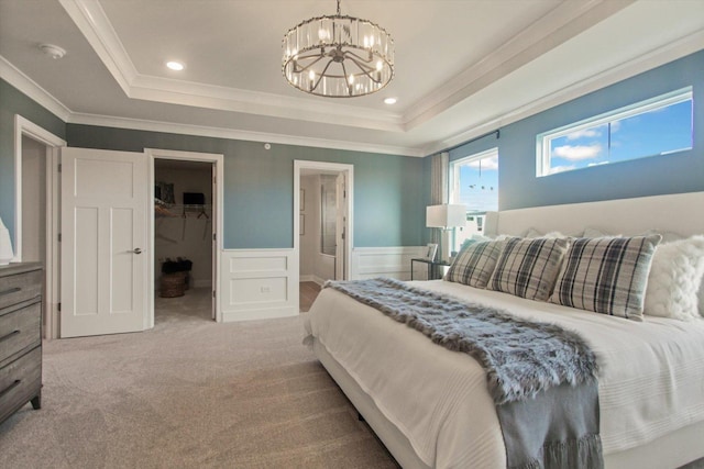 carpeted bedroom featuring a raised ceiling, a wainscoted wall, an inviting chandelier, a walk in closet, and a decorative wall