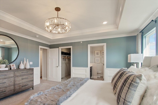 bedroom featuring light carpet, a wainscoted wall, a spacious closet, and a raised ceiling