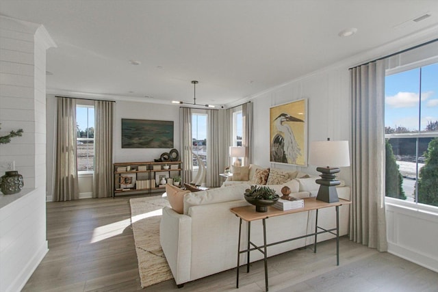 living area with ornamental molding, visible vents, and wood finished floors