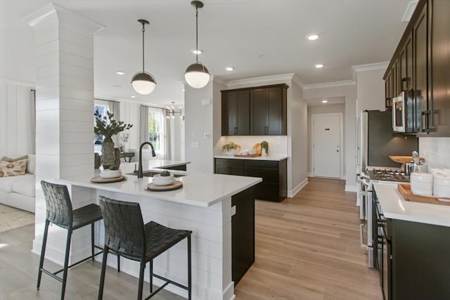 kitchen with a breakfast bar area, a sink, light countertops, appliances with stainless steel finishes, and tasteful backsplash