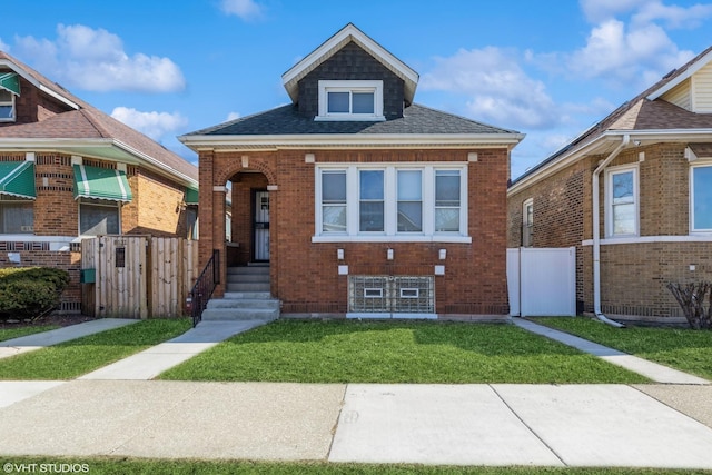 view of front of property with a front lawn, fence, brick siding, and a shingled roof