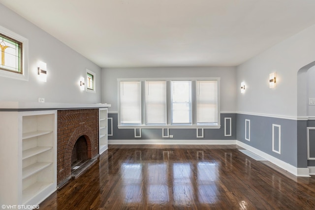 unfurnished living room with built in features, a wealth of natural light, wood finished floors, and a fireplace