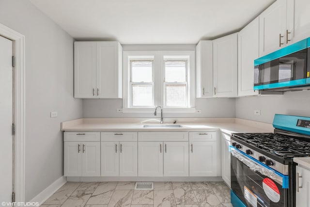 kitchen with gas range, white cabinets, marble finish floor, and a sink