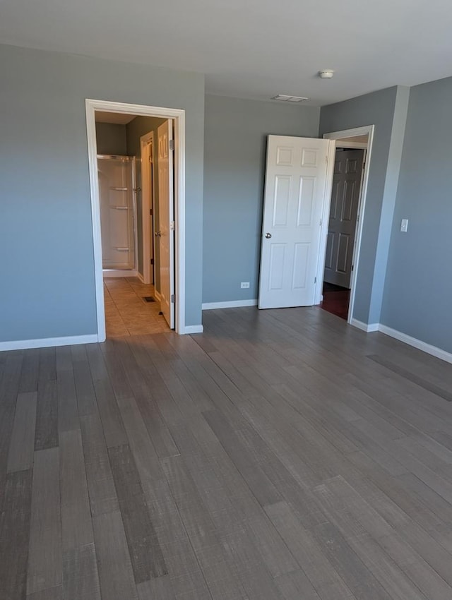 unfurnished bedroom with dark wood-style floors, visible vents, and baseboards