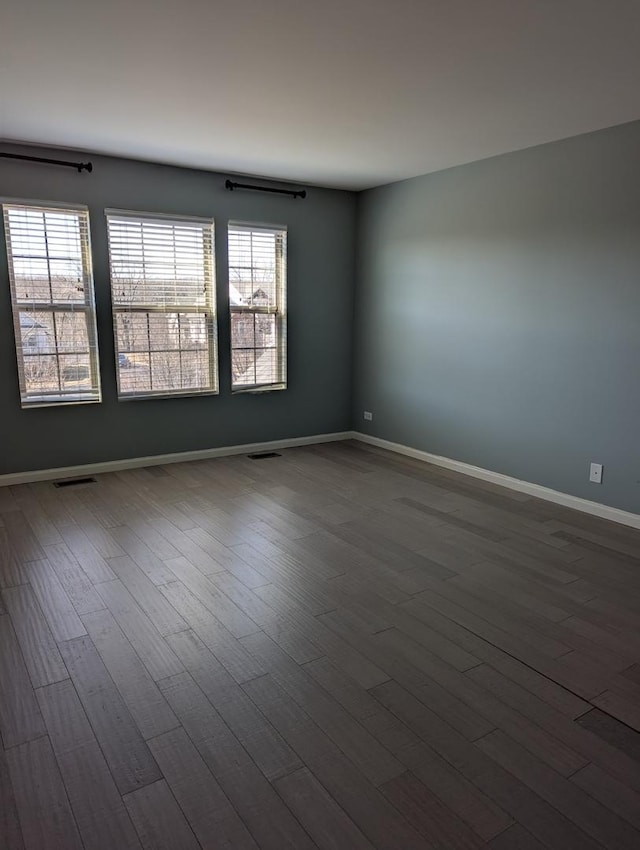 empty room with dark wood-style floors, baseboards, and visible vents