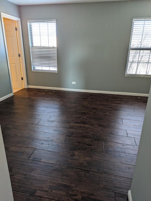 spare room featuring a healthy amount of sunlight, baseboards, and dark wood-type flooring