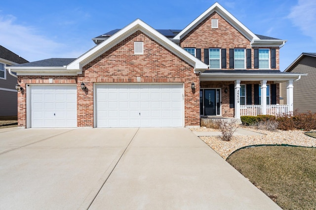 view of front of property featuring brick siding, roof mounted solar panels, covered porch, a garage, and driveway