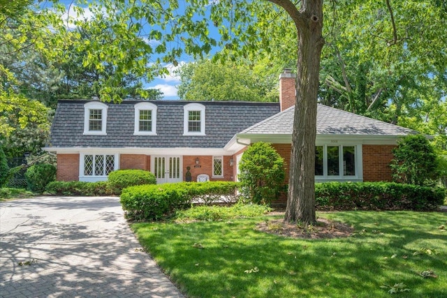 view of front property with brick siding, a front yard, mansard roof, a chimney, and decorative driveway