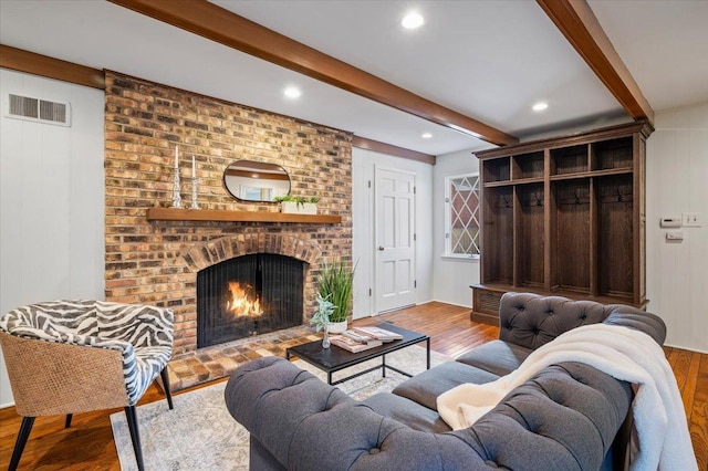 living room with wood finished floors, visible vents, recessed lighting, a brick fireplace, and beamed ceiling