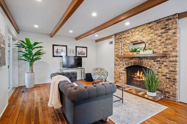 living area with hardwood / wood-style floors, visible vents, beam ceiling, recessed lighting, and a brick fireplace