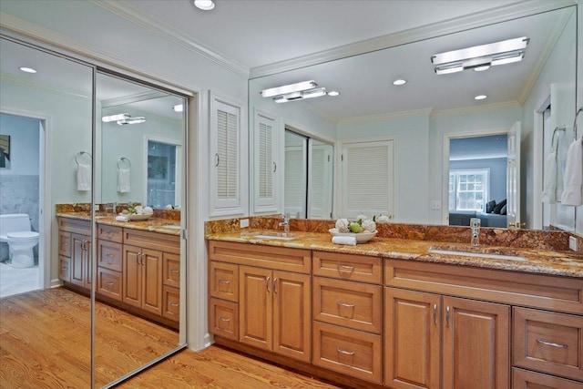 bathroom featuring wood finished floors, double vanity, a sink, crown molding, and toilet