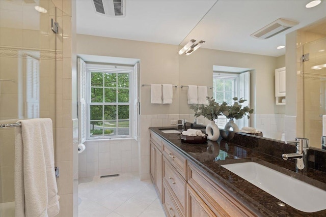 bathroom with tile walls, a stall shower, visible vents, and a sink