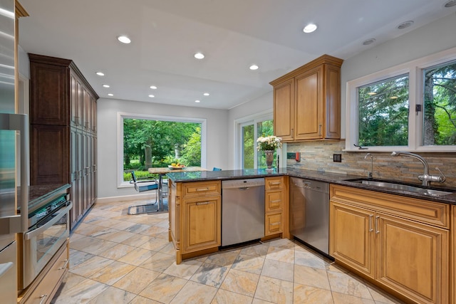 kitchen with a sink, dark stone counters, appliances with stainless steel finishes, a peninsula, and decorative backsplash