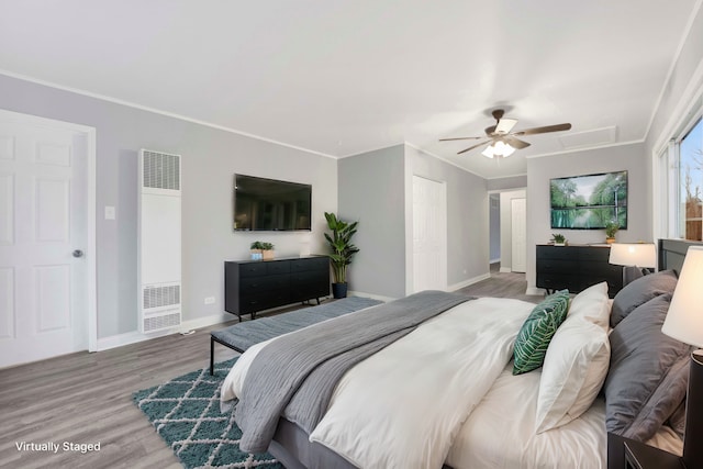 bedroom featuring ceiling fan, wood finished floors, baseboards, a heating unit, and crown molding