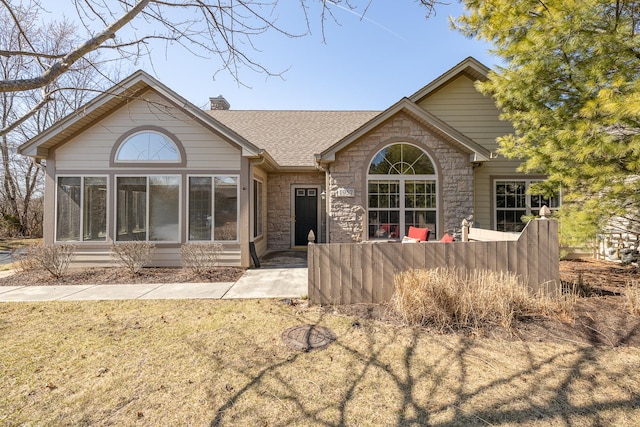 ranch-style house with stone siding, a chimney, roof with shingles, and a sunroom