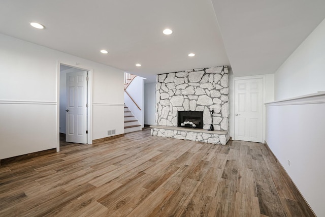 unfurnished living room with wood finished floors, visible vents, recessed lighting, a stone fireplace, and stairs