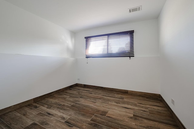 empty room with dark wood finished floors, visible vents, and baseboards