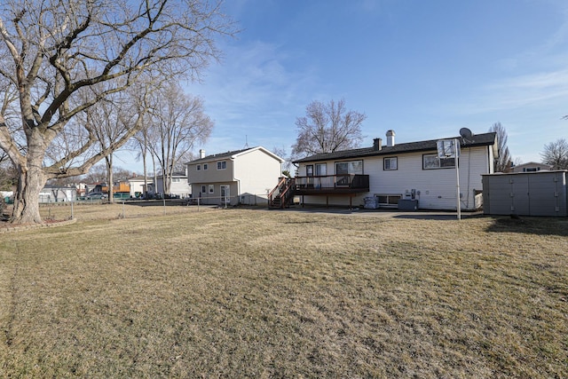 rear view of house featuring fence, a lawn, a deck, an outdoor structure, and a storage unit