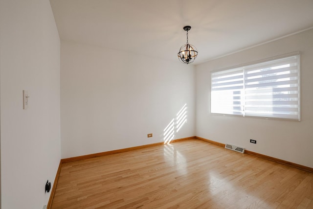 unfurnished room with visible vents, a notable chandelier, and light wood finished floors