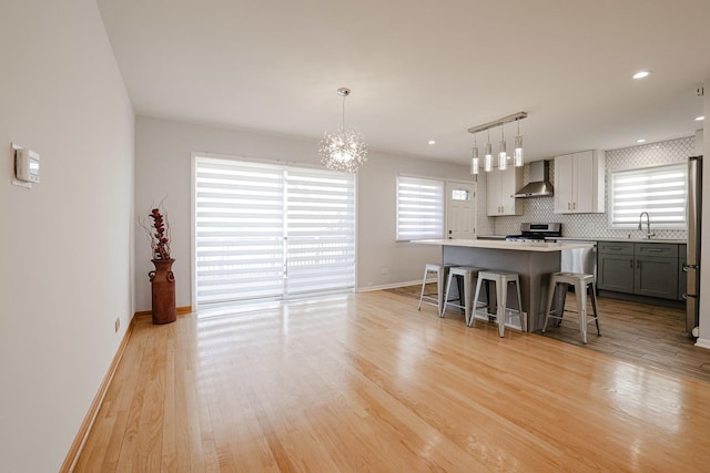 kitchen with light wood finished floors, decorative backsplash, stainless steel range, a kitchen breakfast bar, and wall chimney exhaust hood