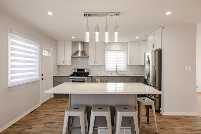 kitchen with a breakfast bar area, decorative backsplash, light wood-style floors, stainless steel appliances, and wall chimney exhaust hood