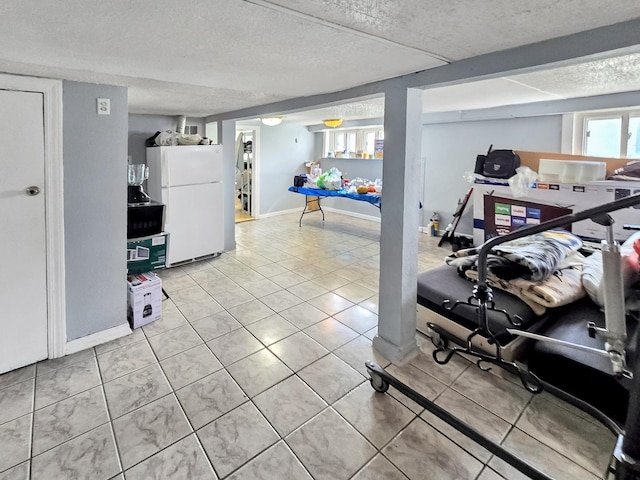 exercise room with a textured ceiling, light tile patterned floors, and baseboards