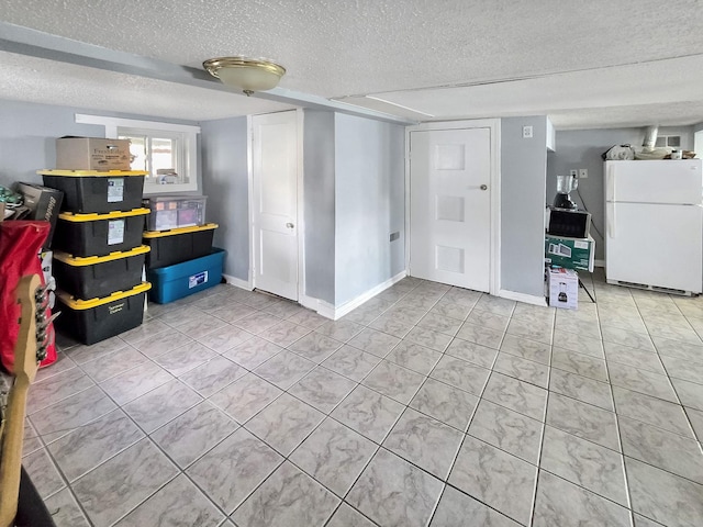 basement featuring light tile patterned flooring, baseboards, a textured ceiling, and freestanding refrigerator