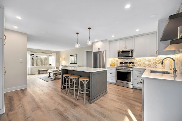 kitchen featuring light countertops, backsplash, appliances with stainless steel finishes, a sink, and a kitchen breakfast bar