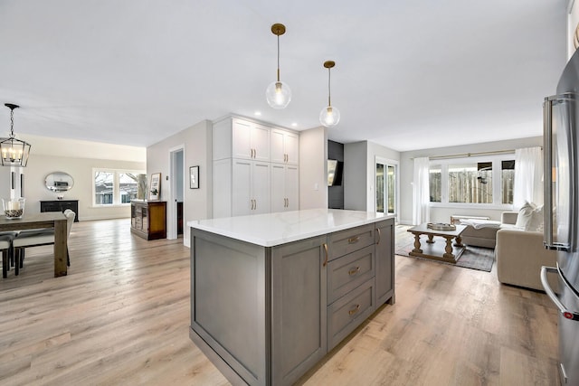 kitchen featuring light wood finished floors, a kitchen island, open floor plan, light stone countertops, and gray cabinets