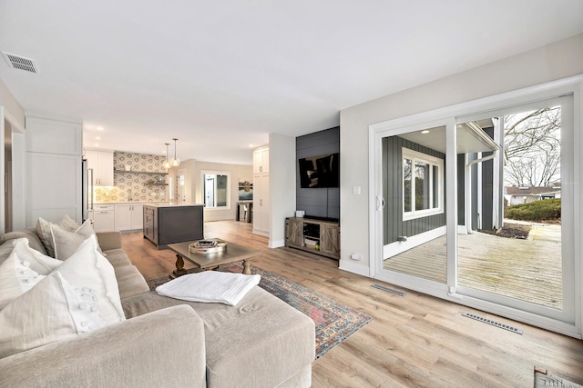 living area with light wood-type flooring, visible vents, and baseboards