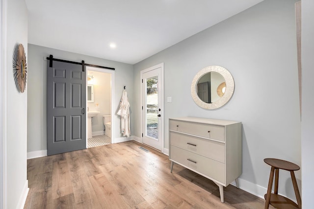 foyer with a barn door, light wood-type flooring, visible vents, and baseboards