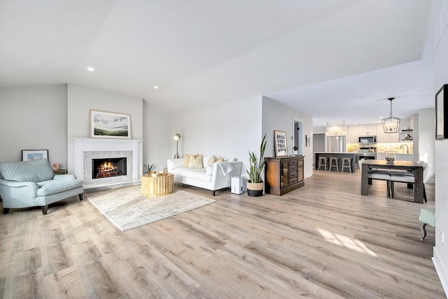 living room with a warm lit fireplace, light wood finished floors, a notable chandelier, and recessed lighting