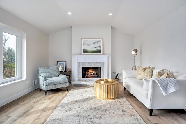 living room featuring lofted ceiling, recessed lighting, light wood-style flooring, a high end fireplace, and baseboards