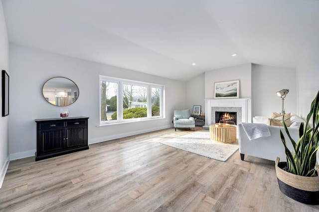 living area featuring lofted ceiling, a lit fireplace, wood finished floors, and baseboards