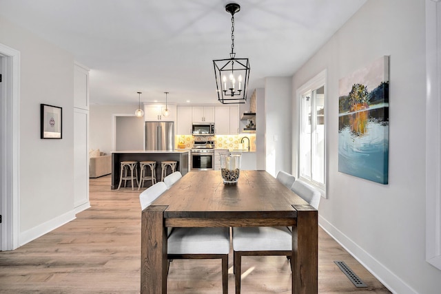 dining room with an inviting chandelier, light wood-style flooring, visible vents, and baseboards