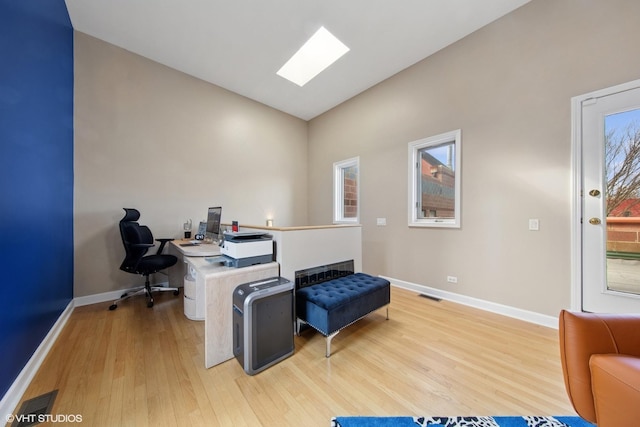 office with visible vents, vaulted ceiling with skylight, baseboards, and wood finished floors