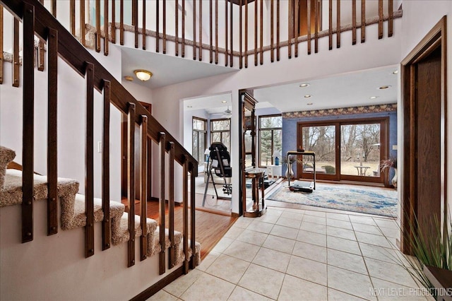 entryway featuring light tile patterned flooring, ceiling fan, stairs, and a towering ceiling