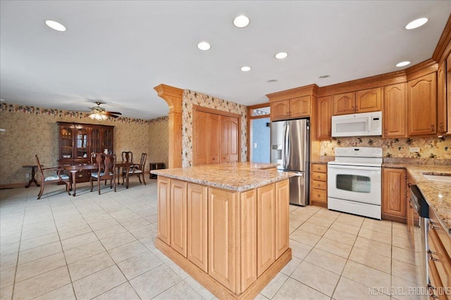 kitchen with a center island, wallpapered walls, ceiling fan, light stone countertops, and appliances with stainless steel finishes