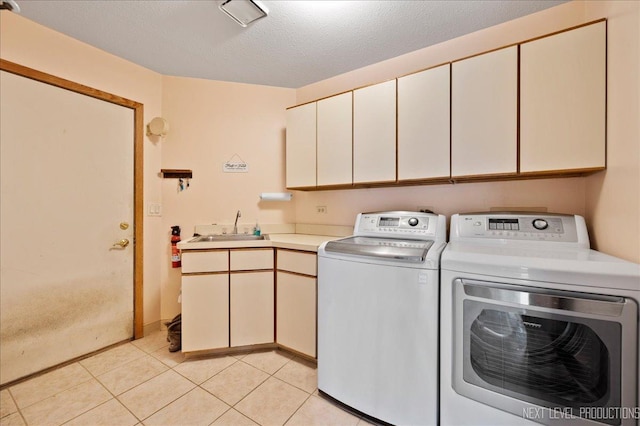 washroom with washer and clothes dryer, a sink, a textured ceiling, cabinet space, and light tile patterned flooring